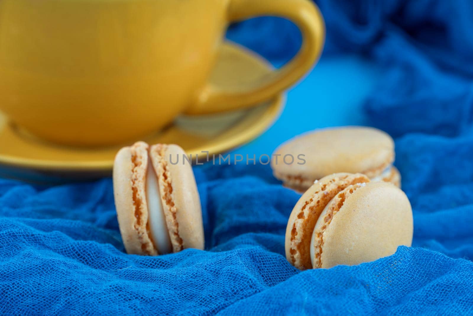 yellow cup of coffee and macaroons on blue background