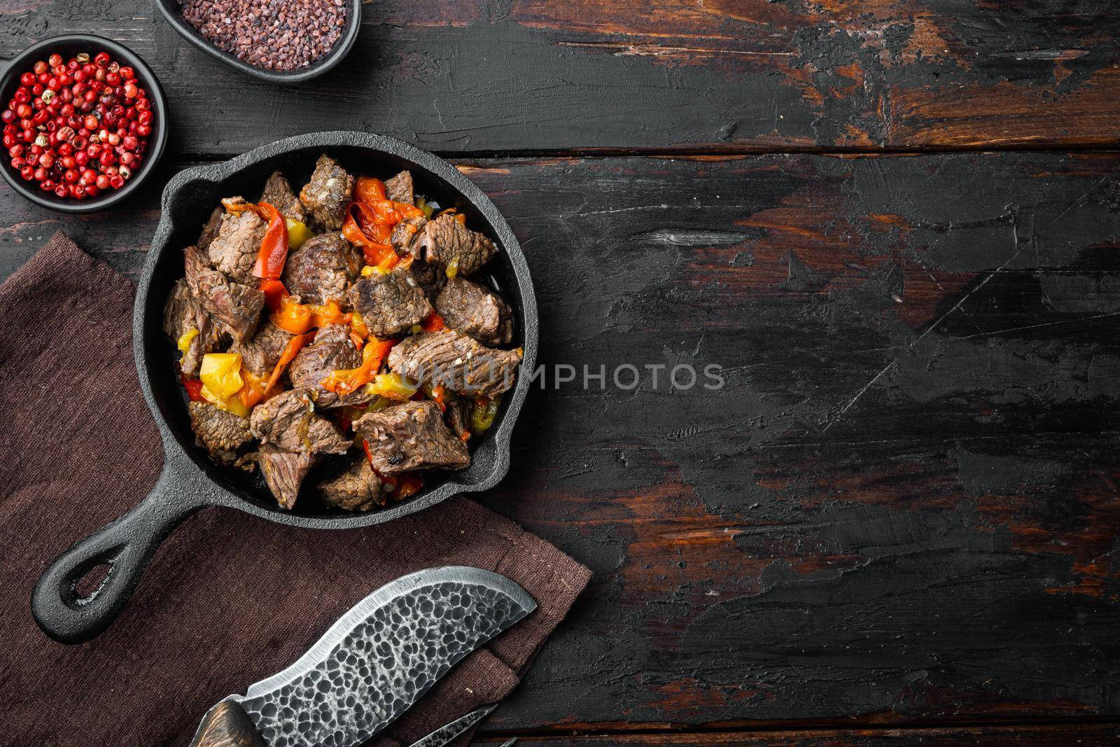 Irish stew made with beef, potatoes, carrots and herbs set, in cast iron frying pan, on old dark wooden table, top view flat lay, with copy space for text