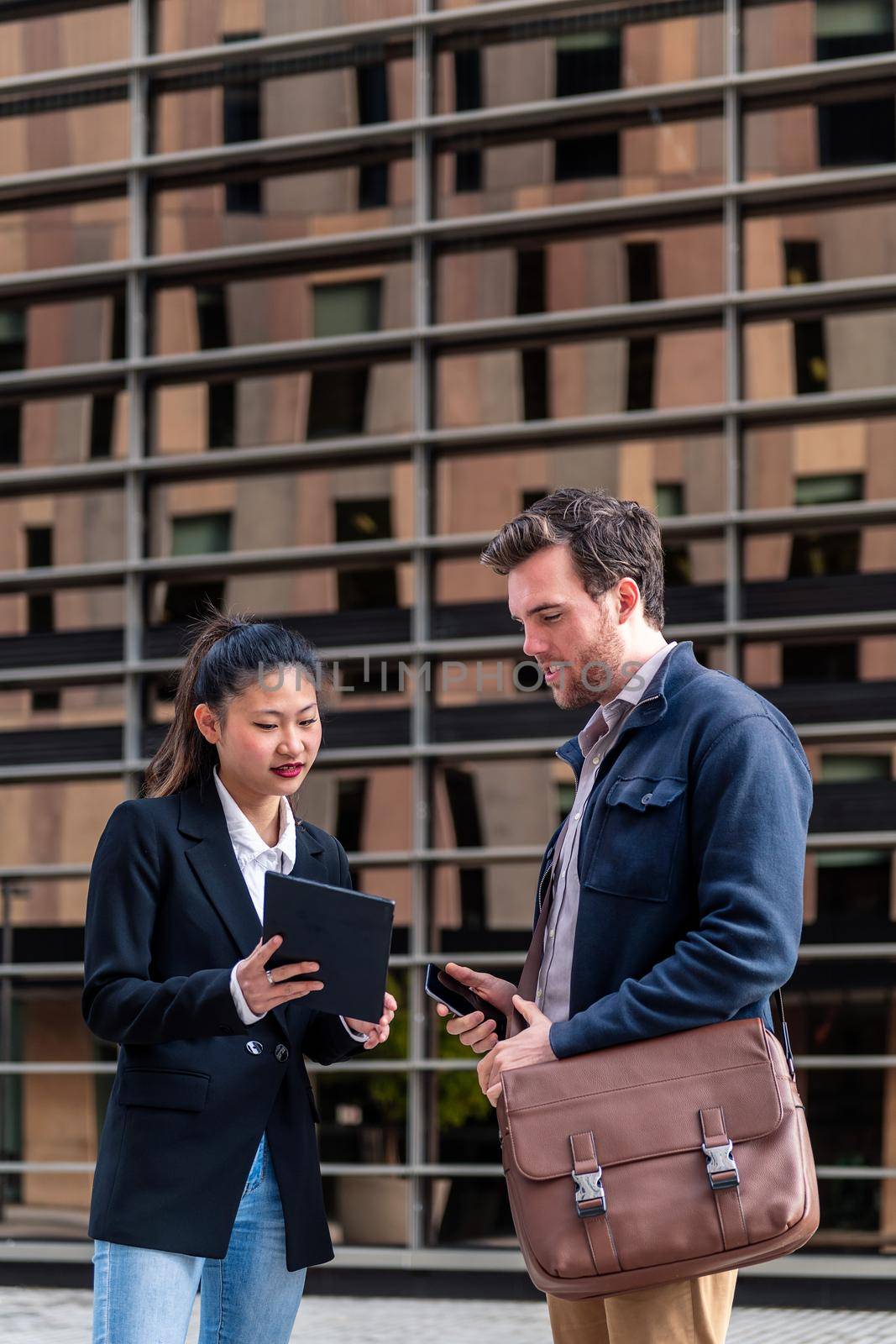 young businesswoman showing her tablet to a businessman next to an office building in the financial district, concept of entrepreneurship and business, copy space for text