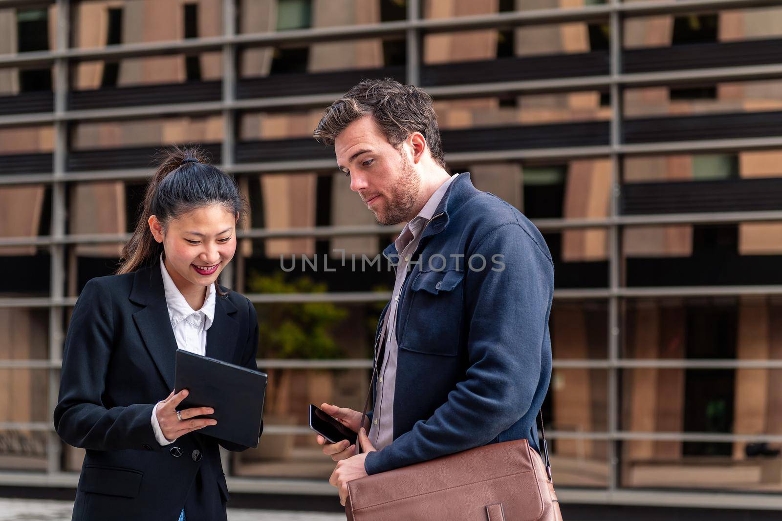 young businesswoman showing her tablet to a businessman next to an office building in the financial district, concept of entrepreneurship and business, copy space for text