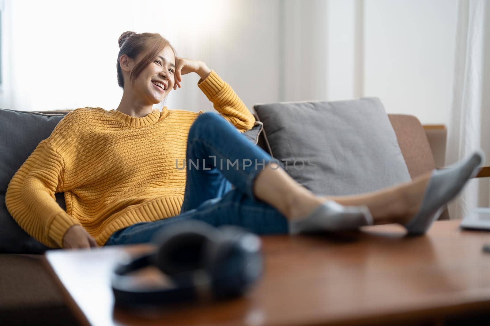 Relaxing home lifestyle happy asian woman in relax room sofa lying back with arms behind head smiling. Asian girl in comfortable lounging chair travel living