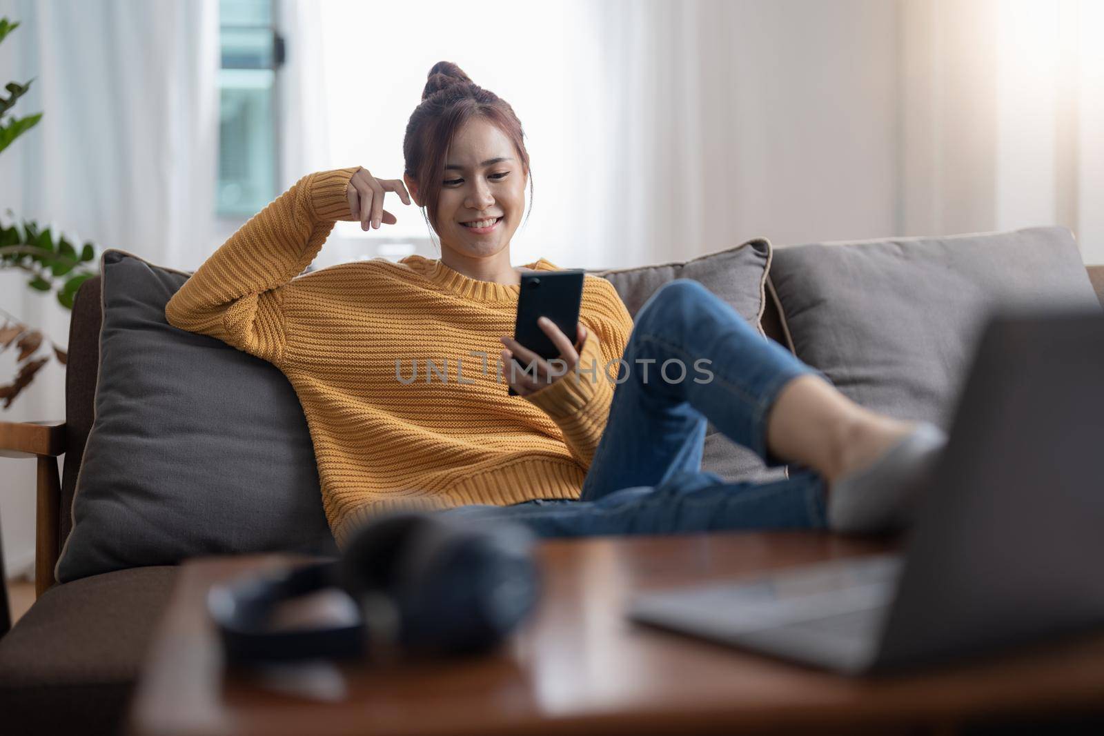 Happy asian teen girl checking social media holding smartphone at home. Smiling young woman using mobile phone app playing game, shopping online, ordering delivery relax on sofa.