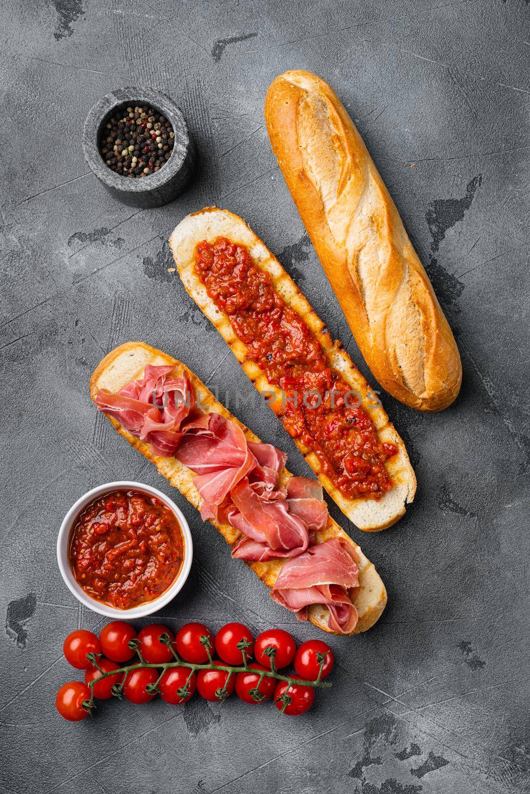 Crusty toast with fresh tomatoes and cured ham, on gray stone table background, top view flat lay