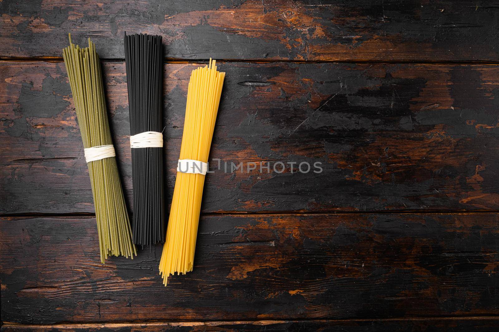 Multi colored spaghetti with ingredients, on old dark wooden table background, top view flat lay, with copy space for text by Ilianesolenyi