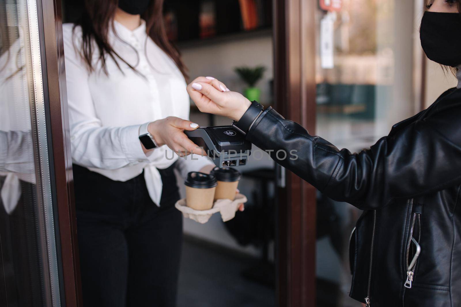 Female customer making wireless or contactless payment using smartwatch. Cashier accepting payment over nfc technology. Two people in face mask during quarantine. Covid19.