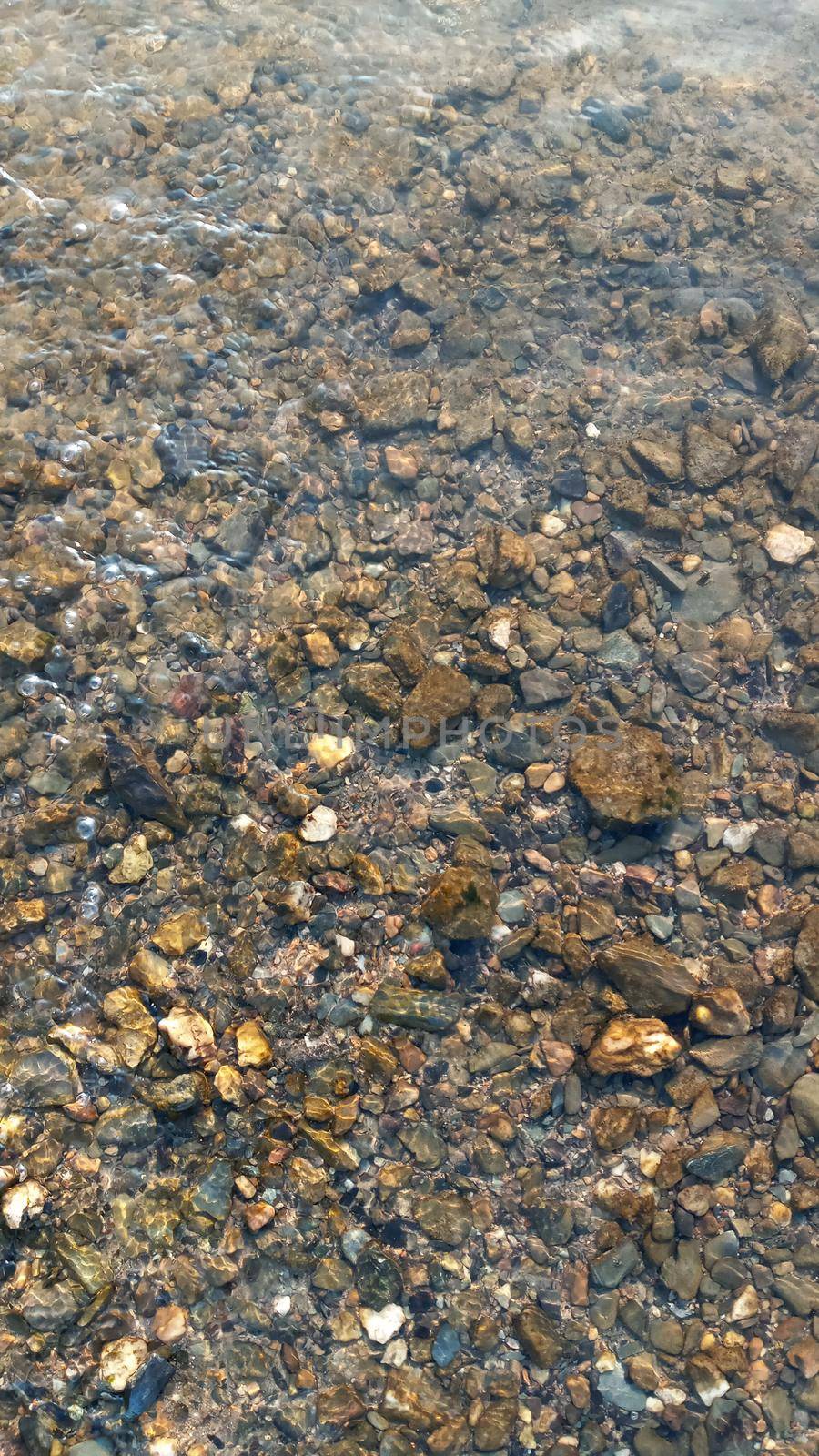 Top view on colorful pebbles covered by water. Close up view of smooth round pebble stones on the beach.