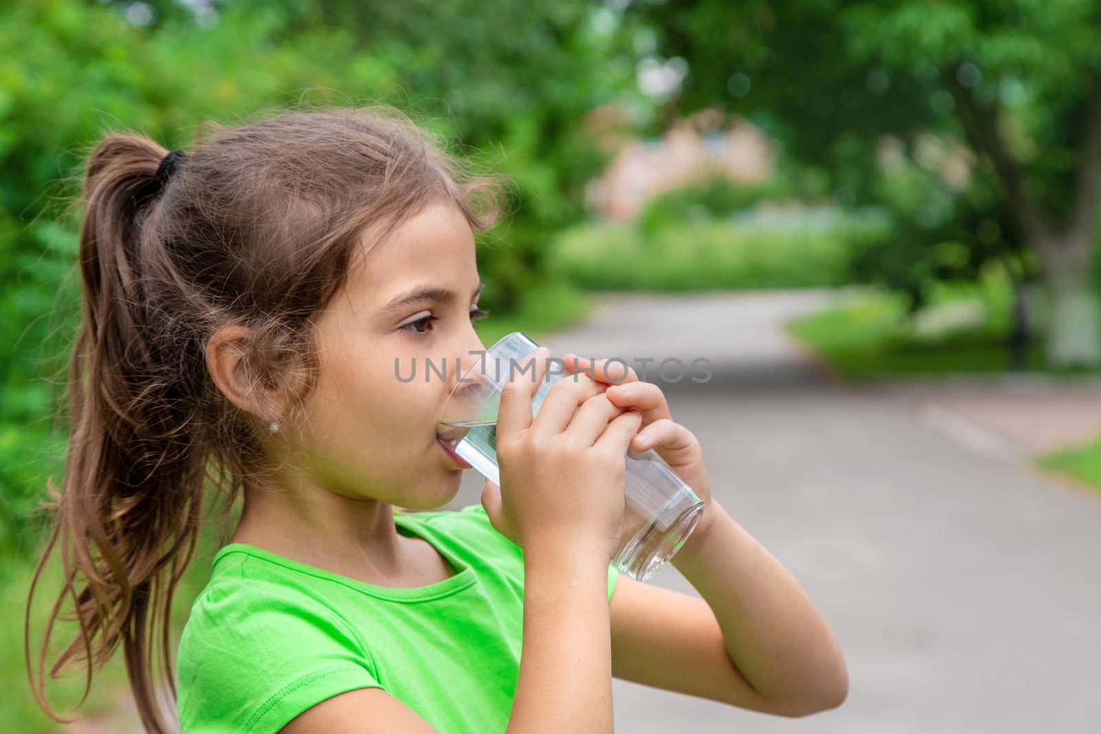 Child girl drinks water from a glass. Selective focus. Kid.