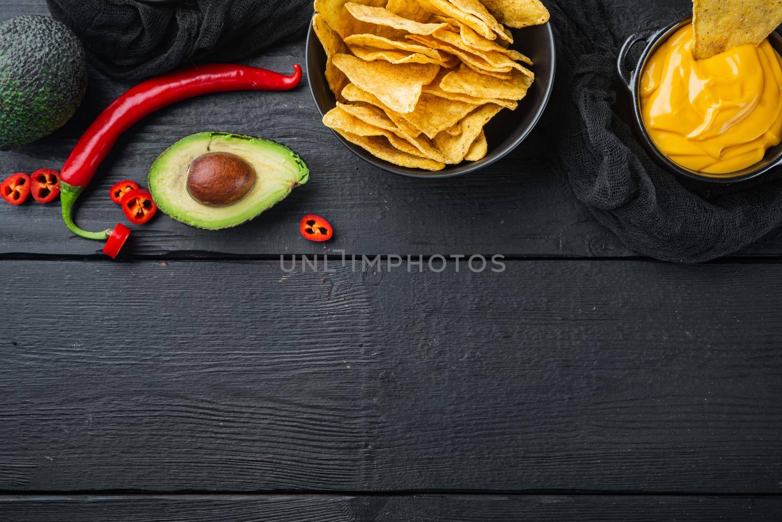 Triangular yellow corn tortilla chip with sauces, on black wooden background, top view or flat lay with copy space for text