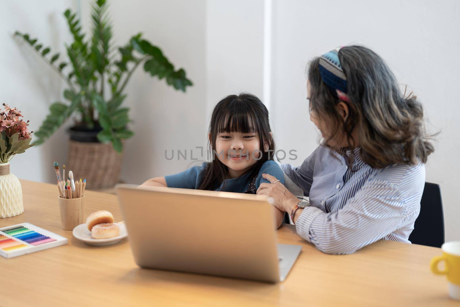 Little girl with grandmother using laptop computer, e learning on virtual online class at home