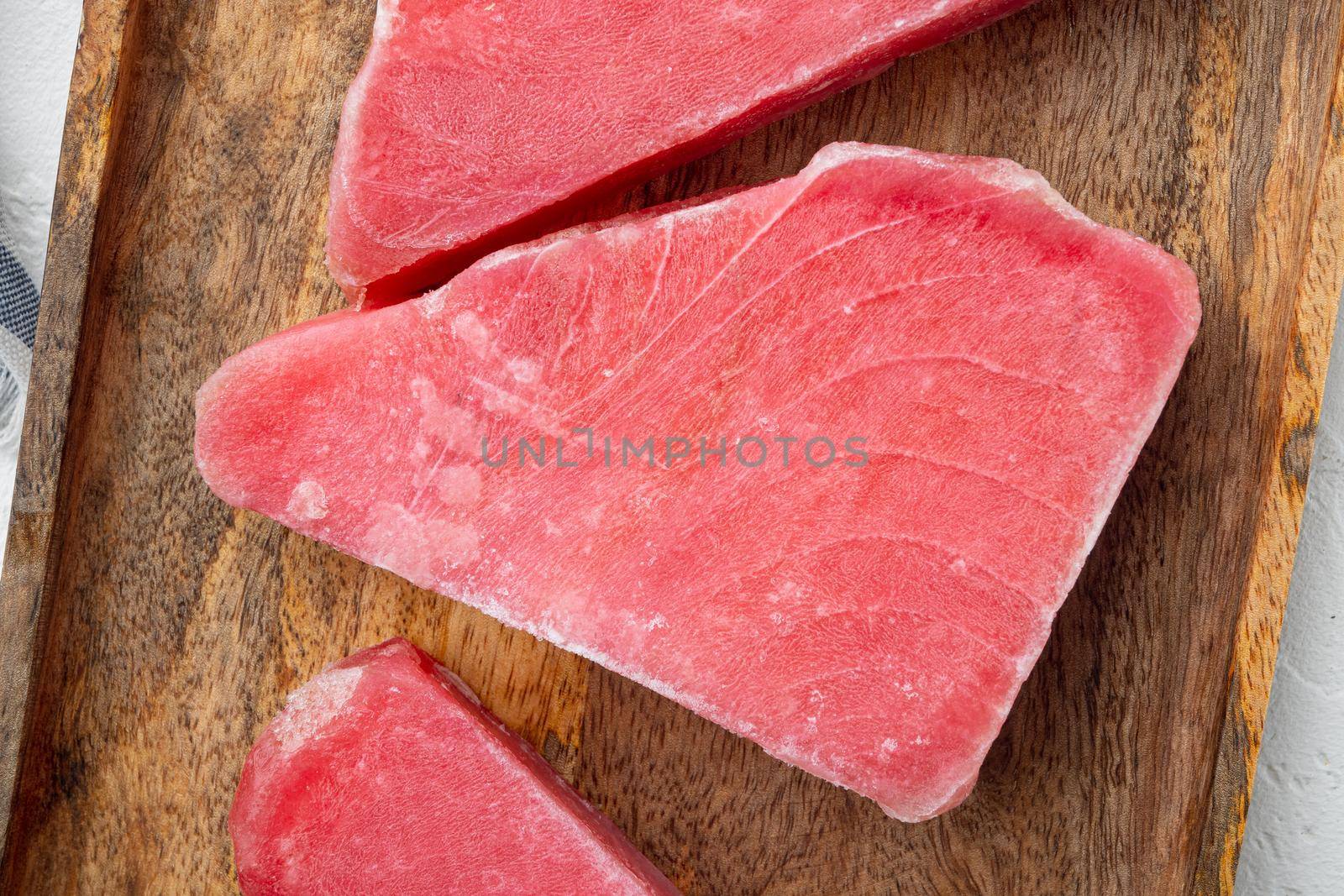 Raw frozen tuna fish fillet set, on wooden tray, on white stone background, top view flat lay