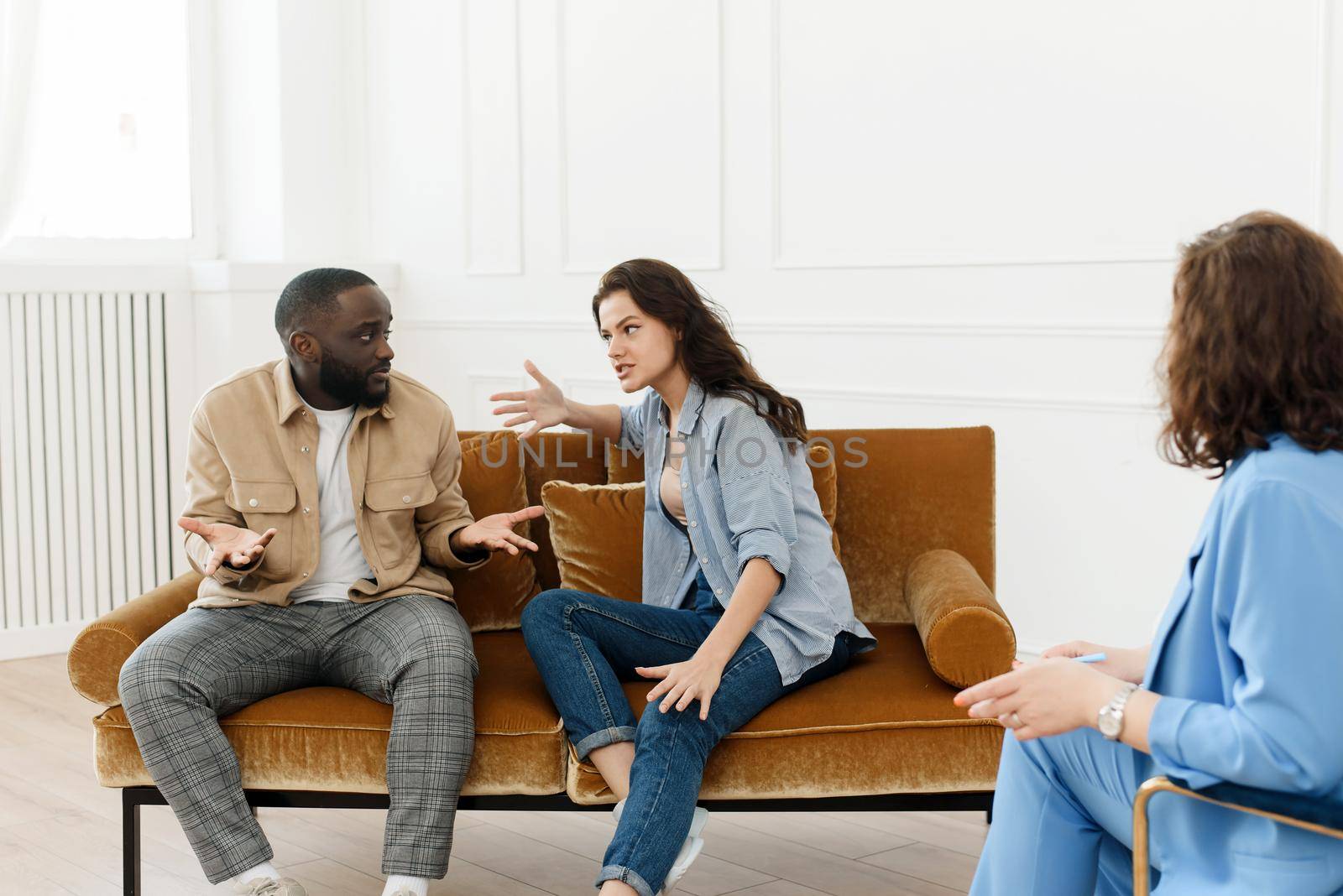 Stressed unhappy millennial Caucasian and African American couple have relationship problems. Diverse couple fighting while visiting professional psychologist for help, breakup prevention concept