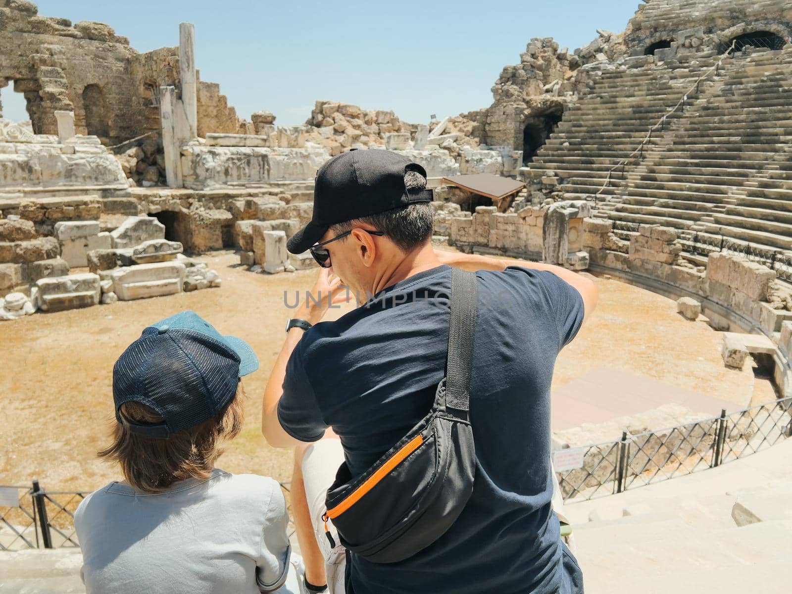 Young father dad and his school boy kid son tourists visiting ancient antique coliseum amphitheater ruins in hot summer day by Ostanina