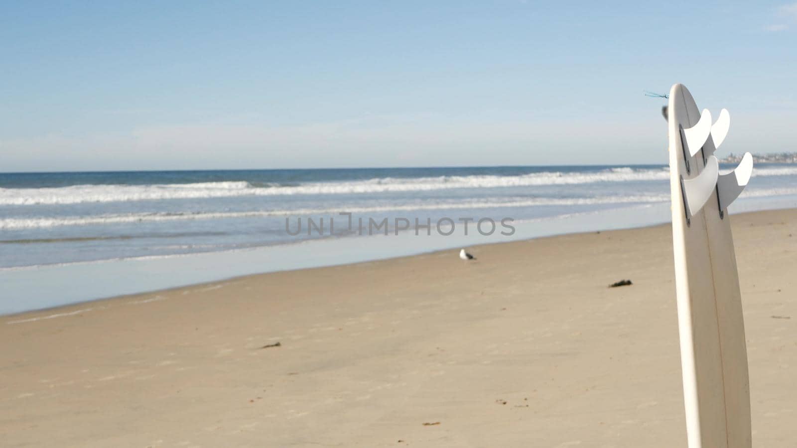 Surfboard for surfing standing on beach sand, California coast, USA. Ocean waves by DogoraSun