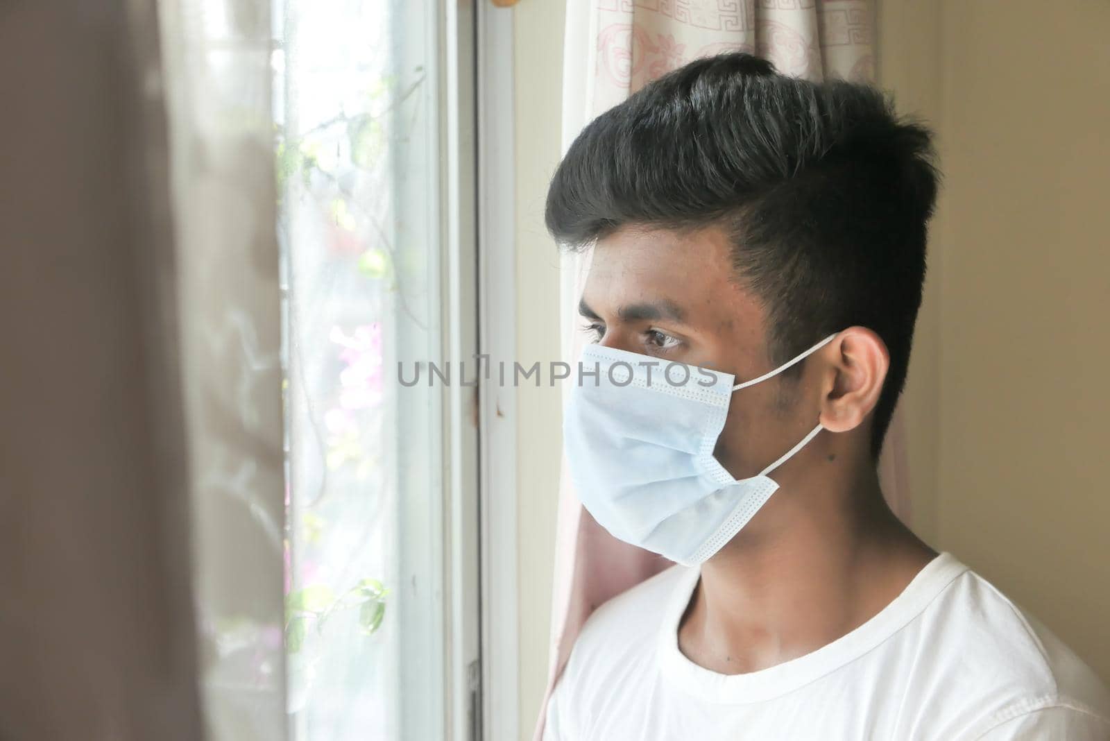 A young man with protective mask looking through window .