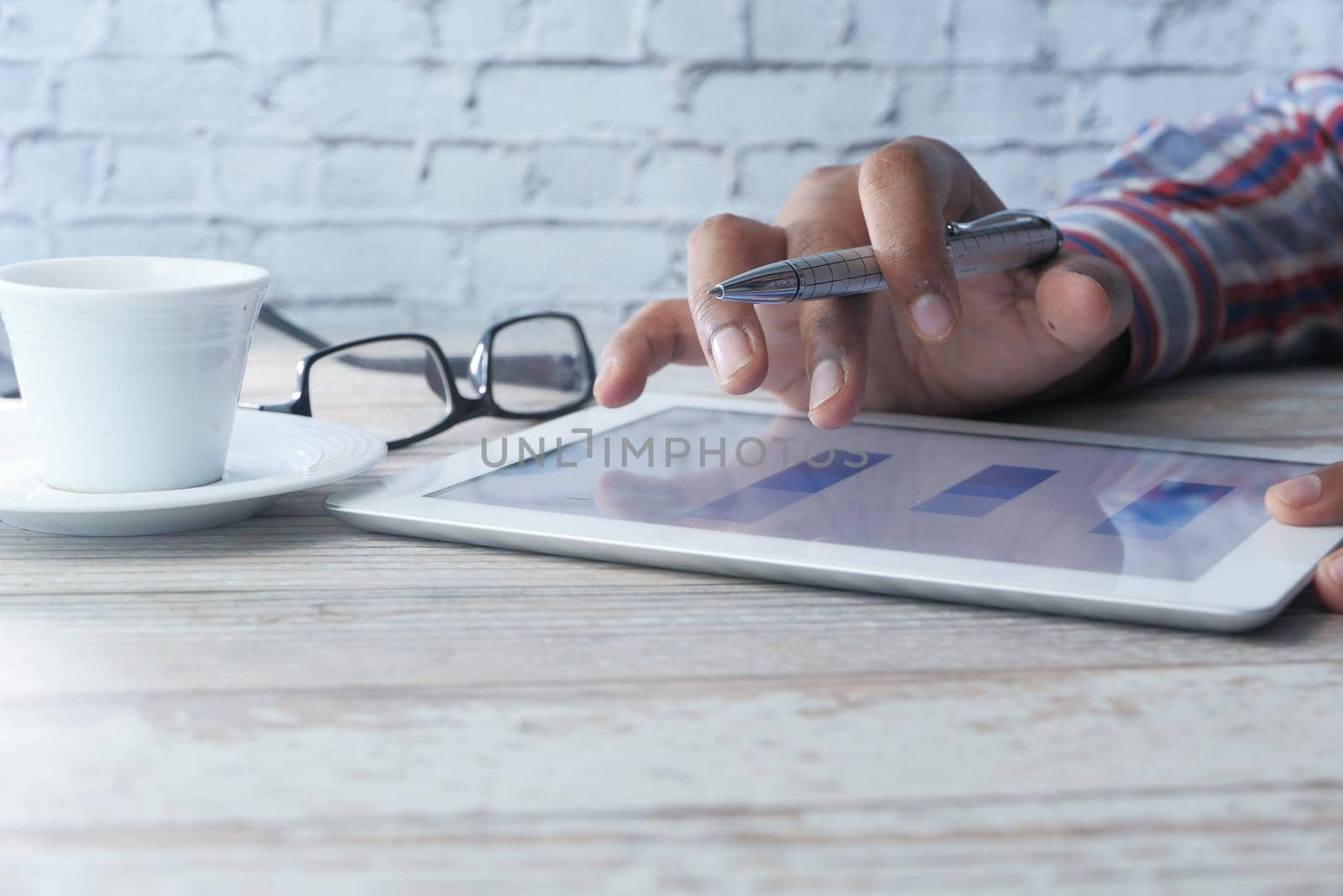 man's hand working on digital tablet at office desk, using self created chart.