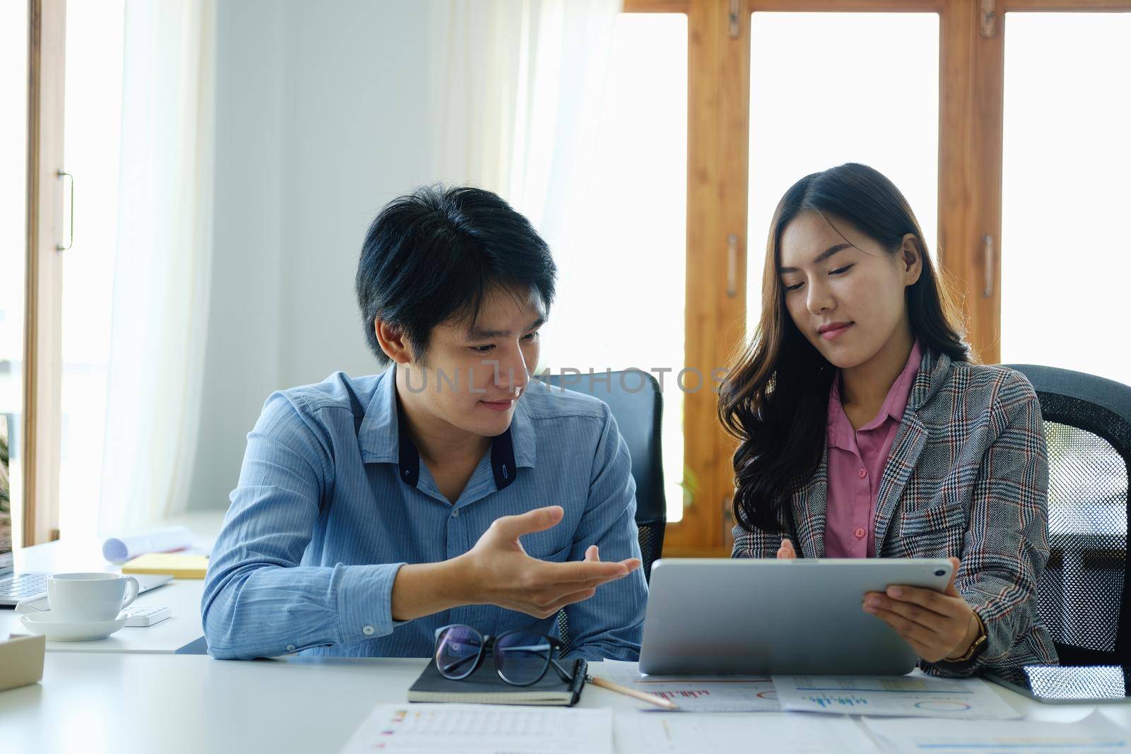 Negotiation, Analysis, Discussion, Asian young economist and marketer using tablet computer to plan investments and financial to prevent risks and losses for the company.