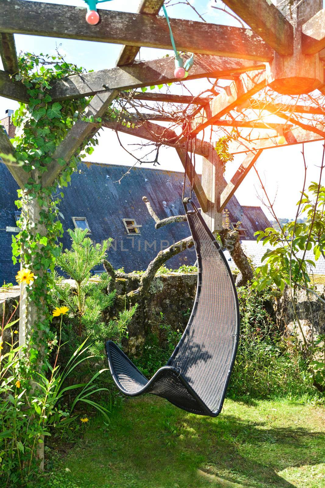Wicker hanging chair in the garden with green nature background and sun