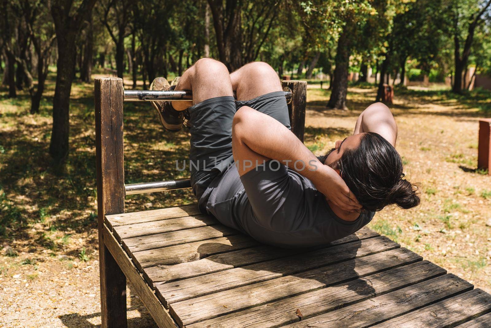 young athletic man doing sit-ups in an outdoor public park. young athlete preparing for a championship. health and wellness lifestyle. Natural sunlight, background of natural vegetation, forest, sportswear.