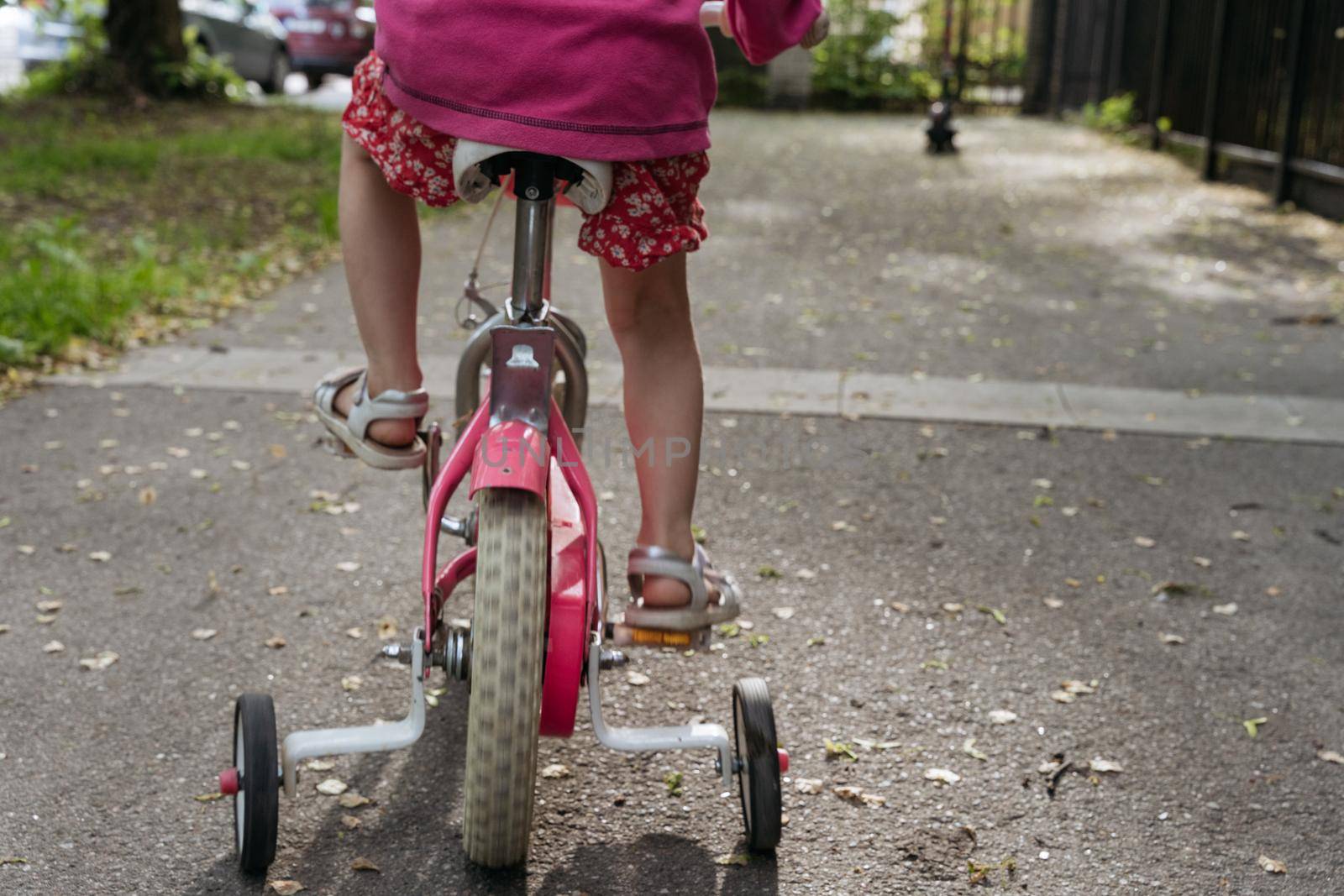 Closeup of girls' feet with white sandals on a pink bike by Varaksina