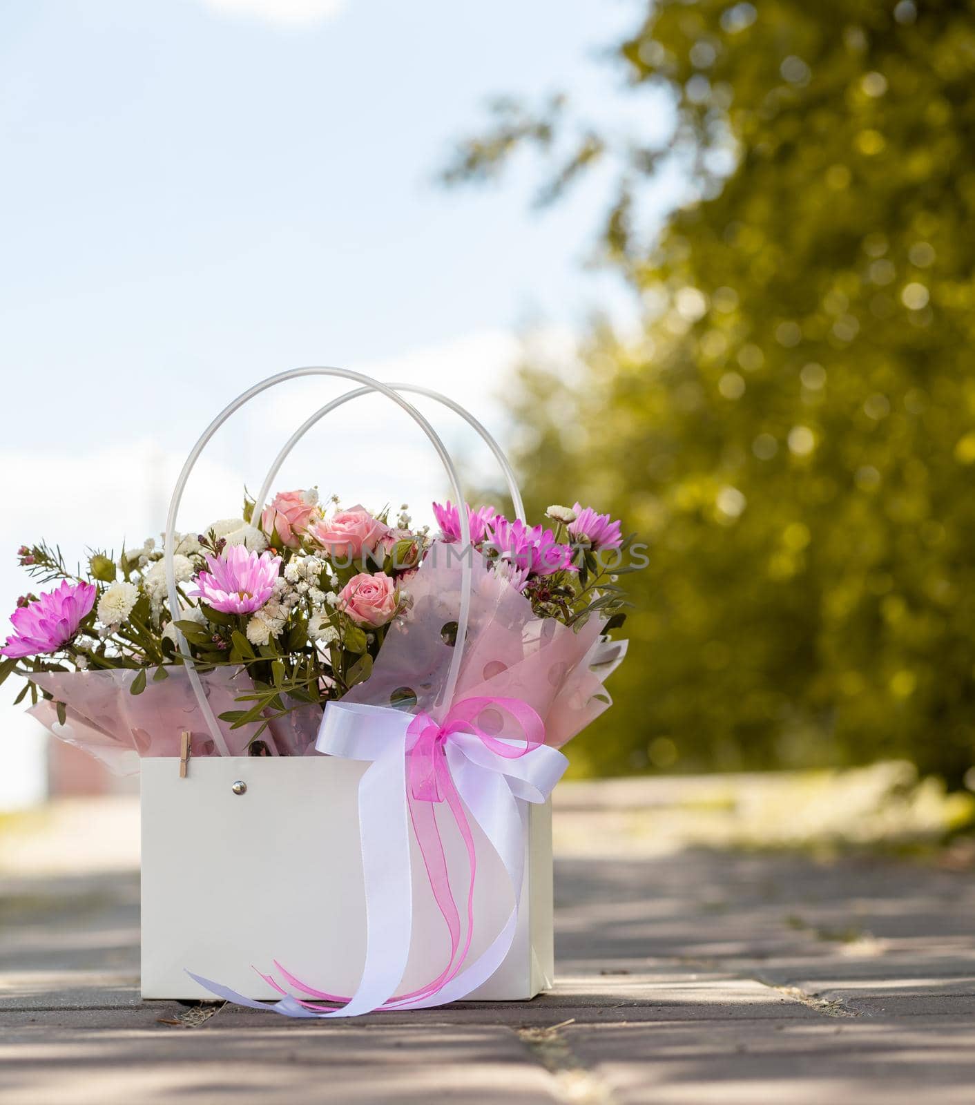 A beautiful bouquet of flowers in a box, which stands on the street as a gift to a beautiful girl who walks along the street on a sunny day. Focus on the background of flowers.