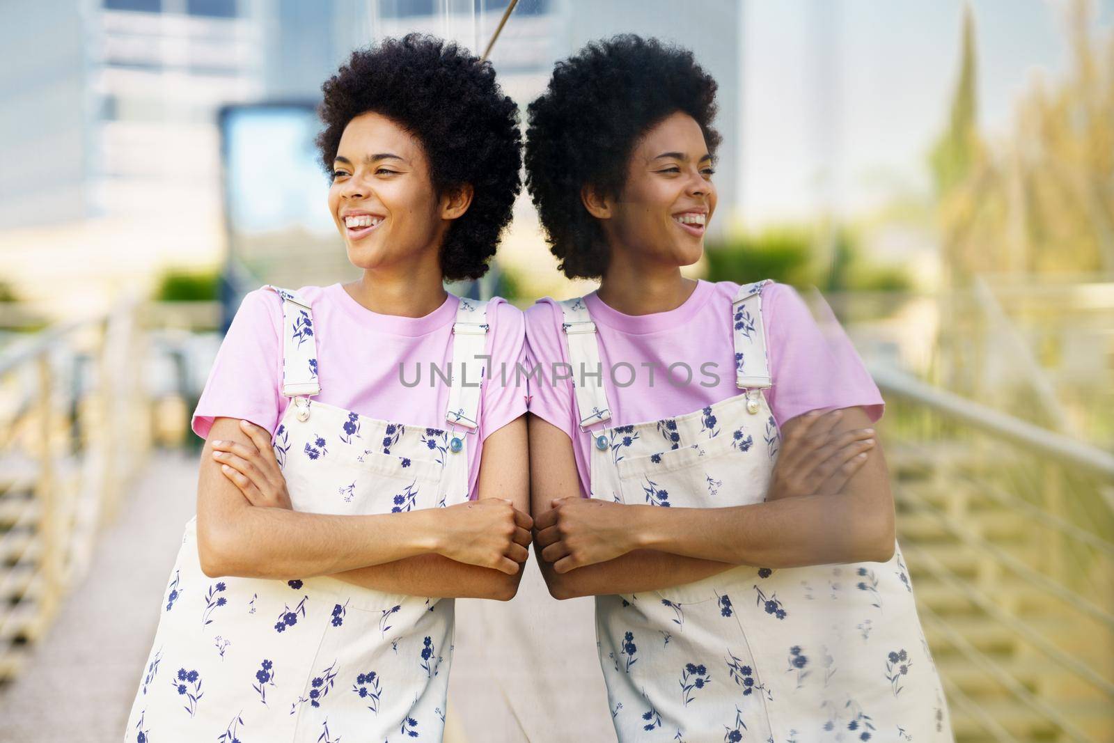 Cheerful black woman in casual clothes laughing in the street. Happy young femeale, afro hair, in urban background.