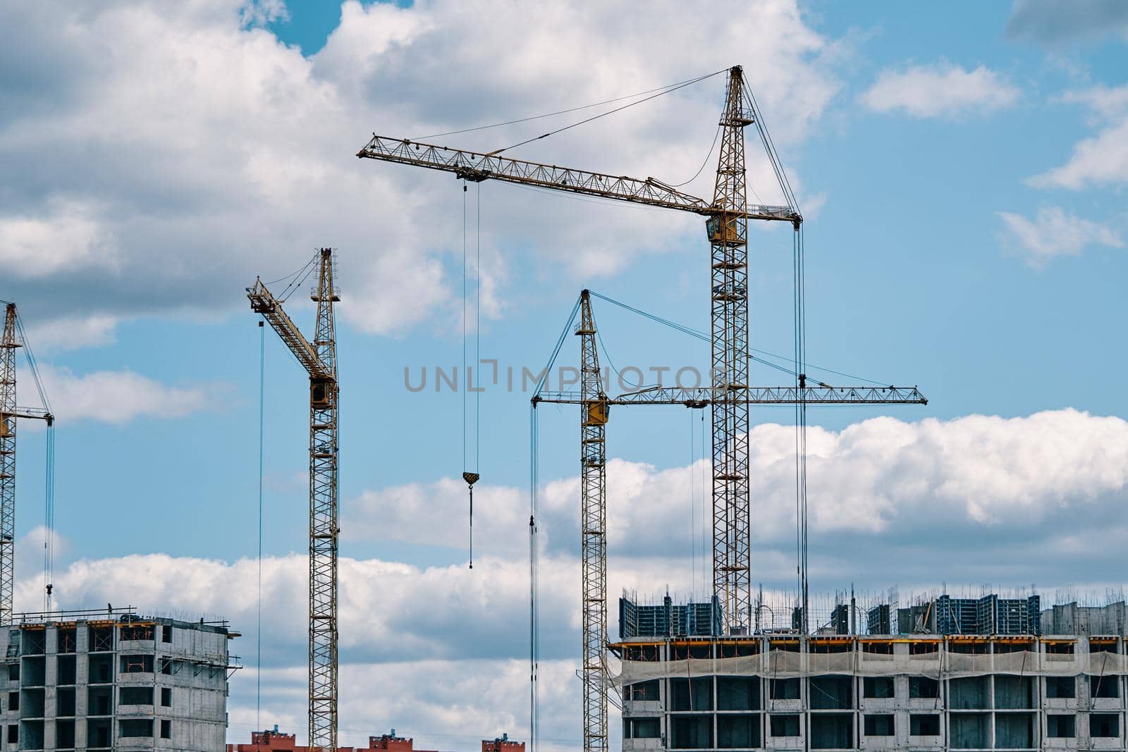 Industrial construction cranes on background of cloudy sky. Hoisting cranes and multi-storey buildings of new city districts. Building site background. Urban area.