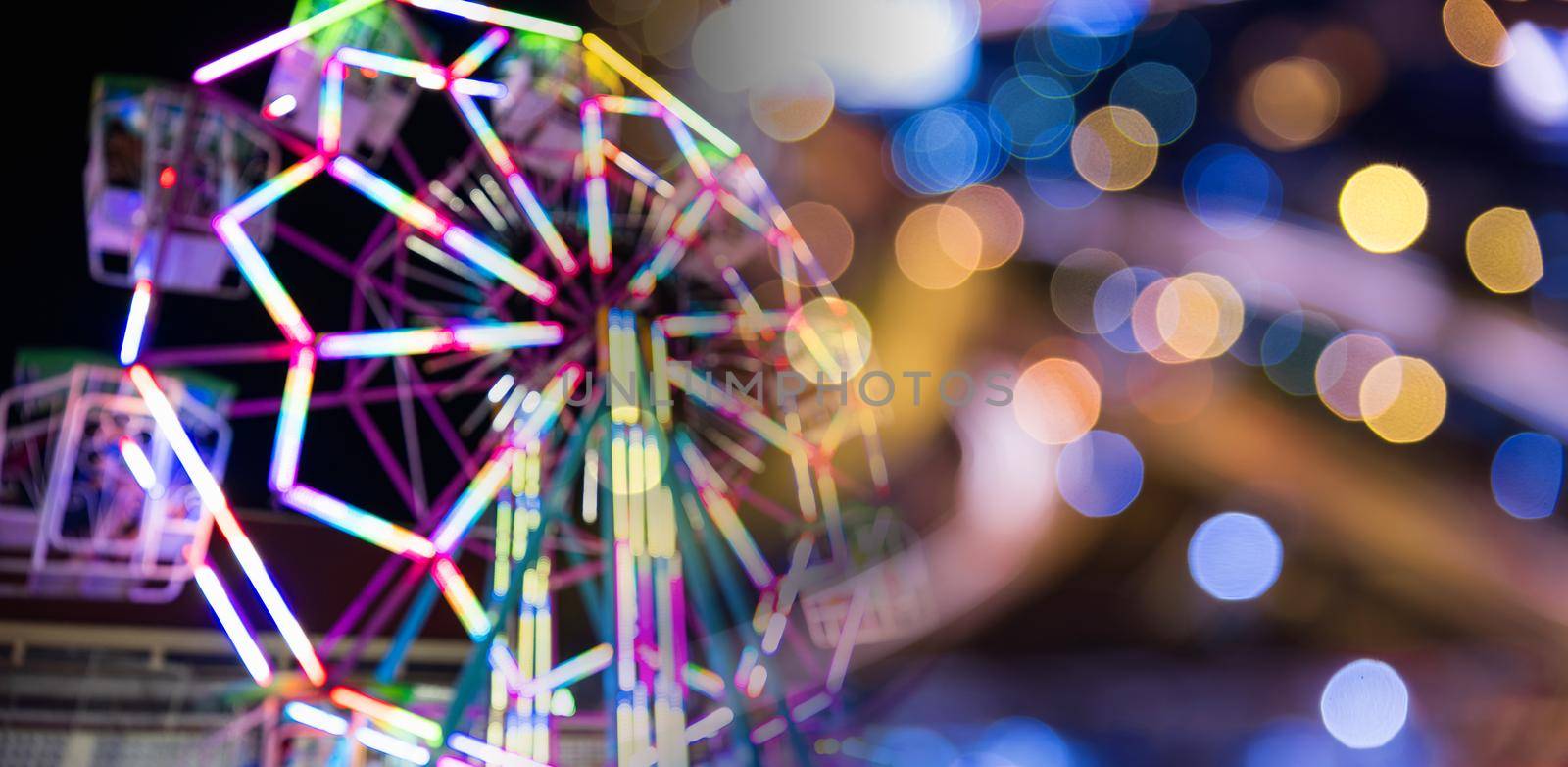 Blurry rollercoaster in bokeh, Ferris wheel at night of colorful with outdoor, Defocused (blurred) and blur image of Amusement park, The annual temple event has activities. Image out of focus