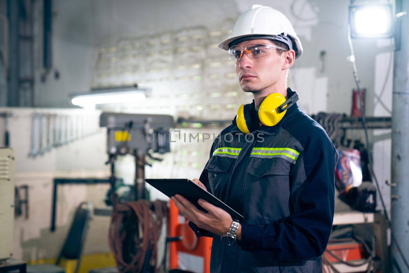 Young factory worker using adept tablet computer in a workshop building . Industrial technology and manufacturing software configuration .