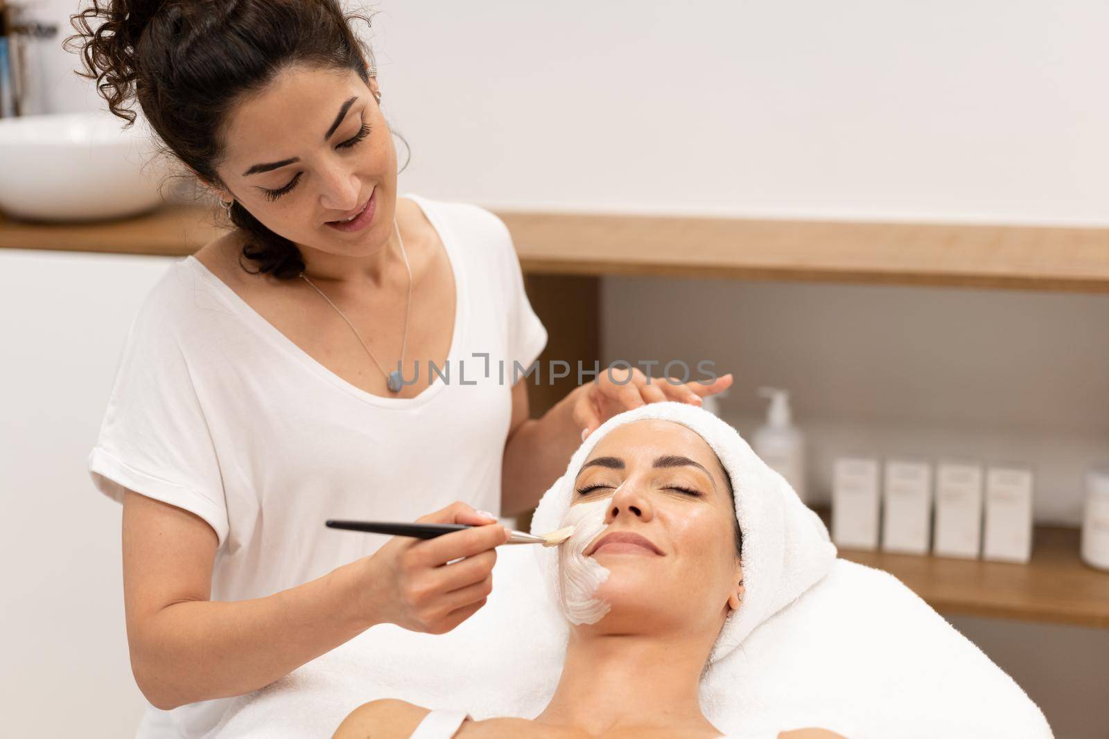 Beautician applying facial mask on client by javiindy