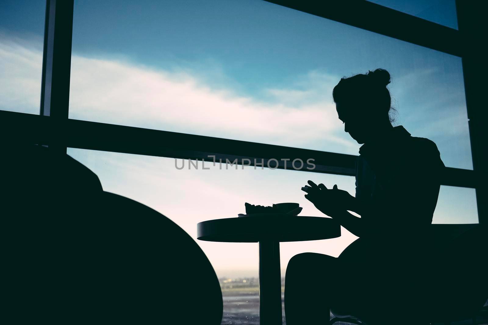 Woman waiting at airport lounge against window sitting at table.