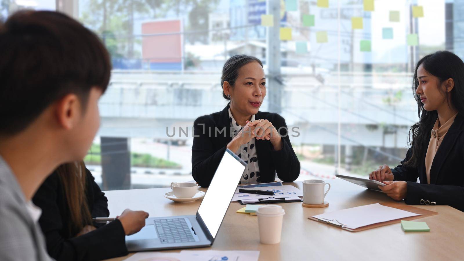 Smiling young female team leader coach discussing market research results to diverse business people at briefing by prathanchorruangsak