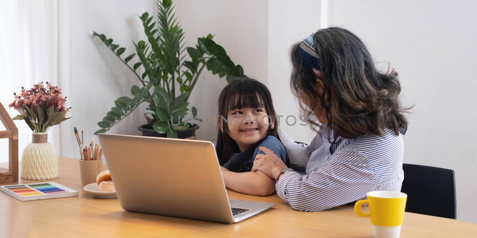 Asian grandmather teach granddaughter drawing and doing homework at home. by wichayada