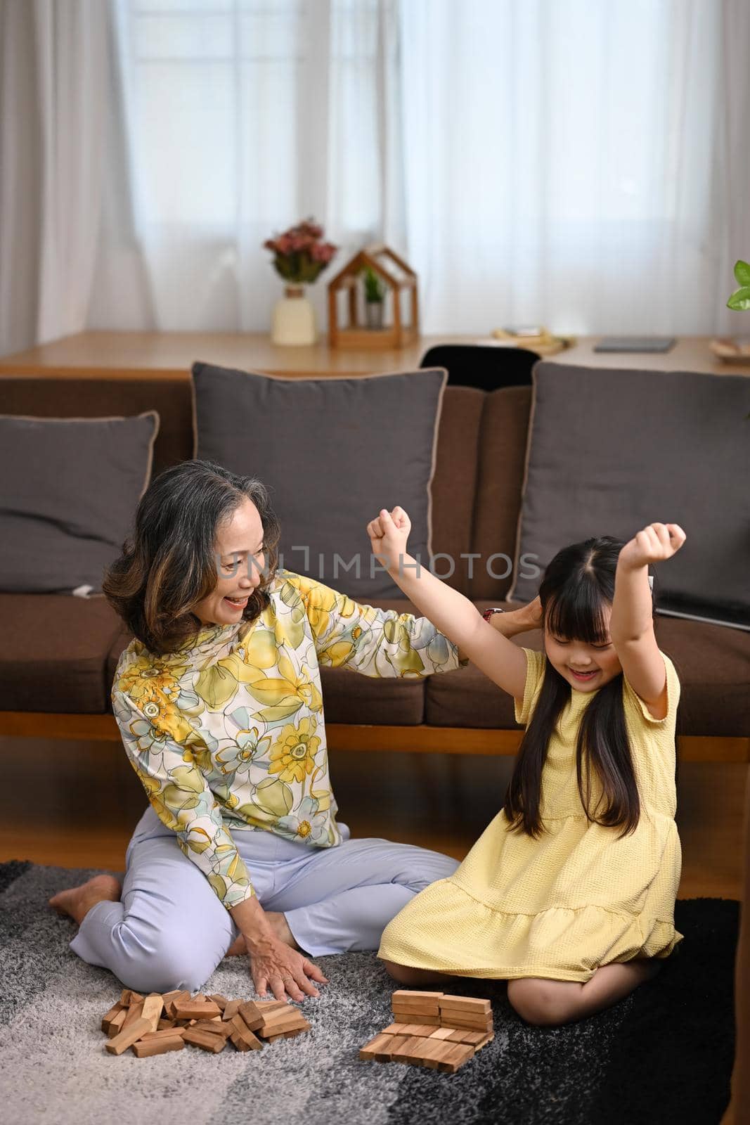 Happy mature grandmother having fun playing with cute little preschooler granddaughter in living room. Multi generational, family and love concept.