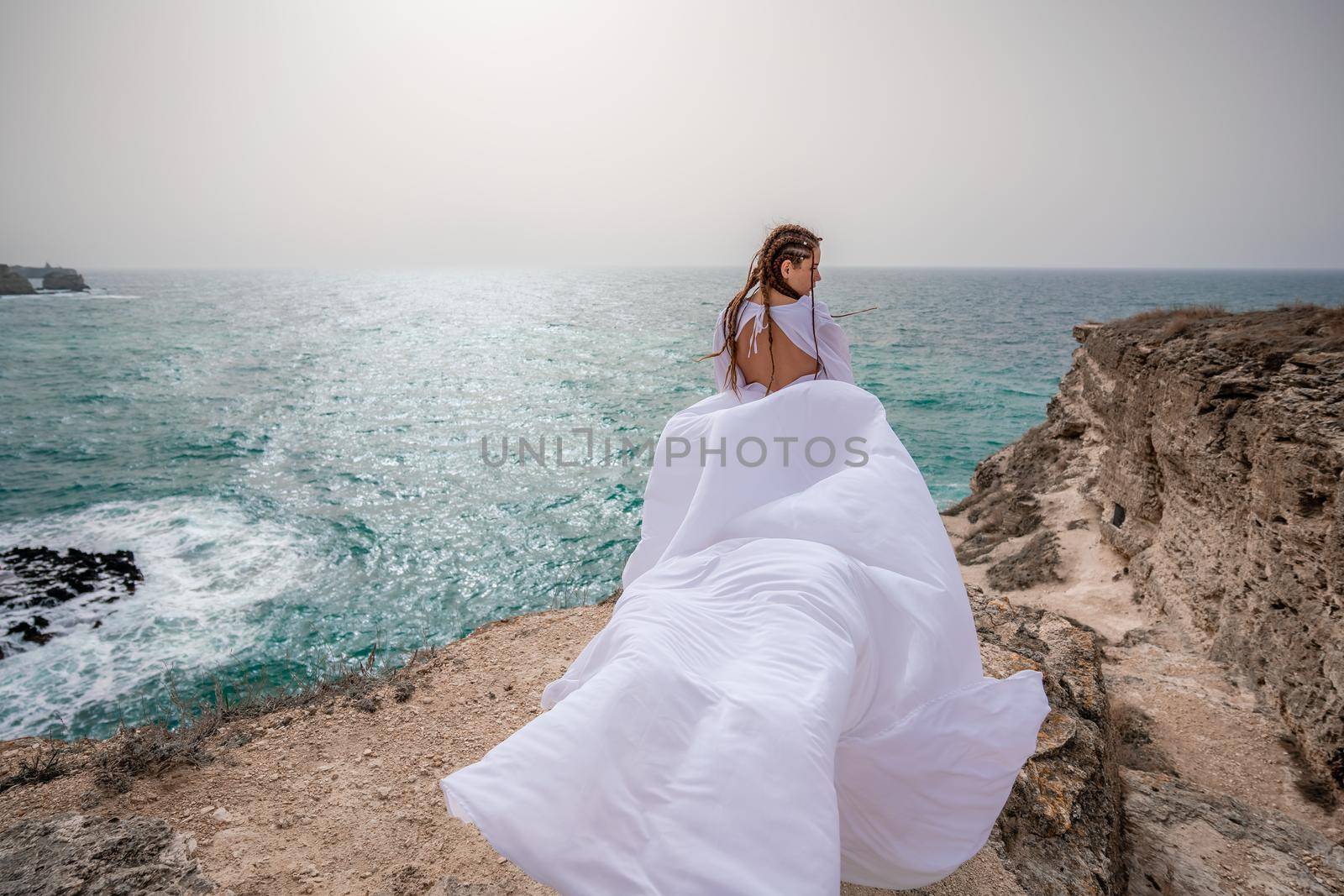 Happy freedom woman on the beach enjoying and posing in white dress. Rear view of a girl in a fluttering white dress in the wind. Holidays, holidays at sea. by Matiunina