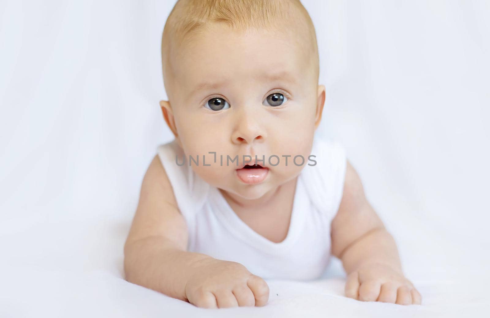 Baby lies on her stomach on a white background. Selective focus. People.