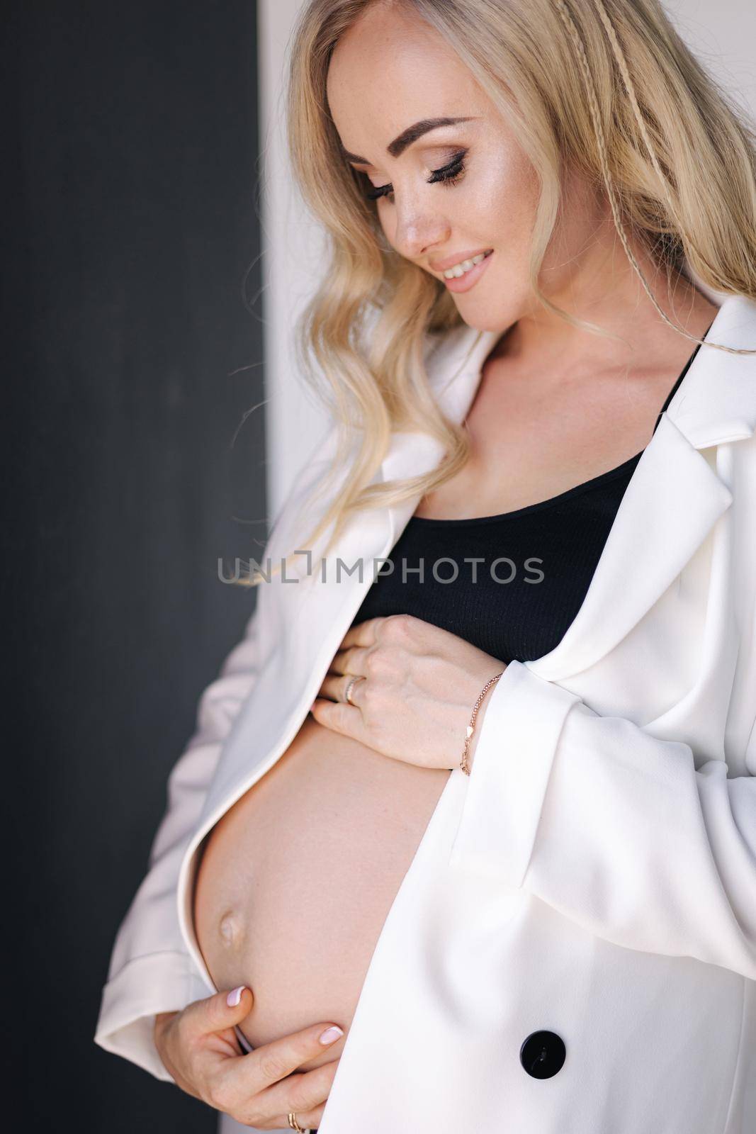 Close up portrait of pregnant woman in studio on white background. Beautiful future mother put her her hands on her belly. Stylish woman in white jaket.