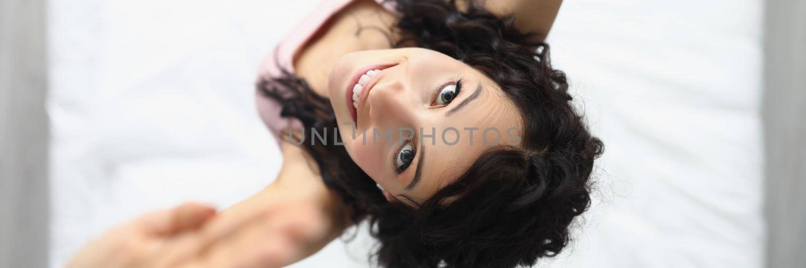 Top view of young cheerful woman jumping on bed after waking up. Create mood in morning for productive day. Good morning, wakeup, fun, happiness concept