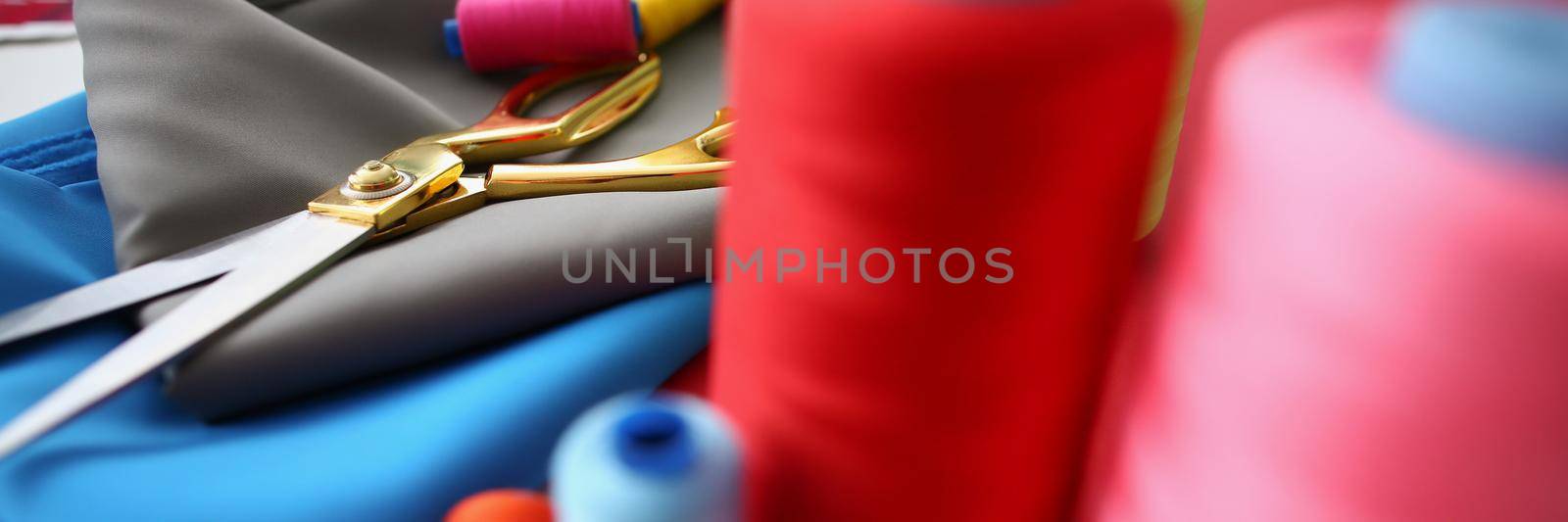 Close-up of composition of sewing accessories scissors and threads on fabric. Creative working atmosphere in private atelier. Business, art, sewing concept