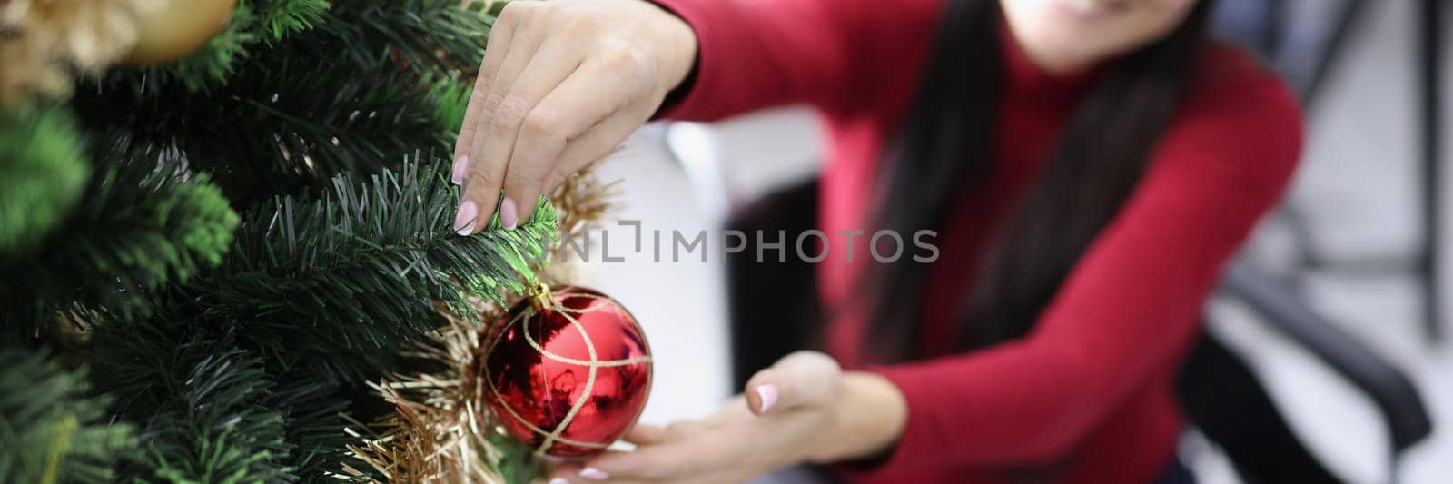 Close-up of woman in wheelchair decorating christmas tree with red ball. Smiling girl in festive mood create cozy atmosphere indoors. Holiday, eve concept