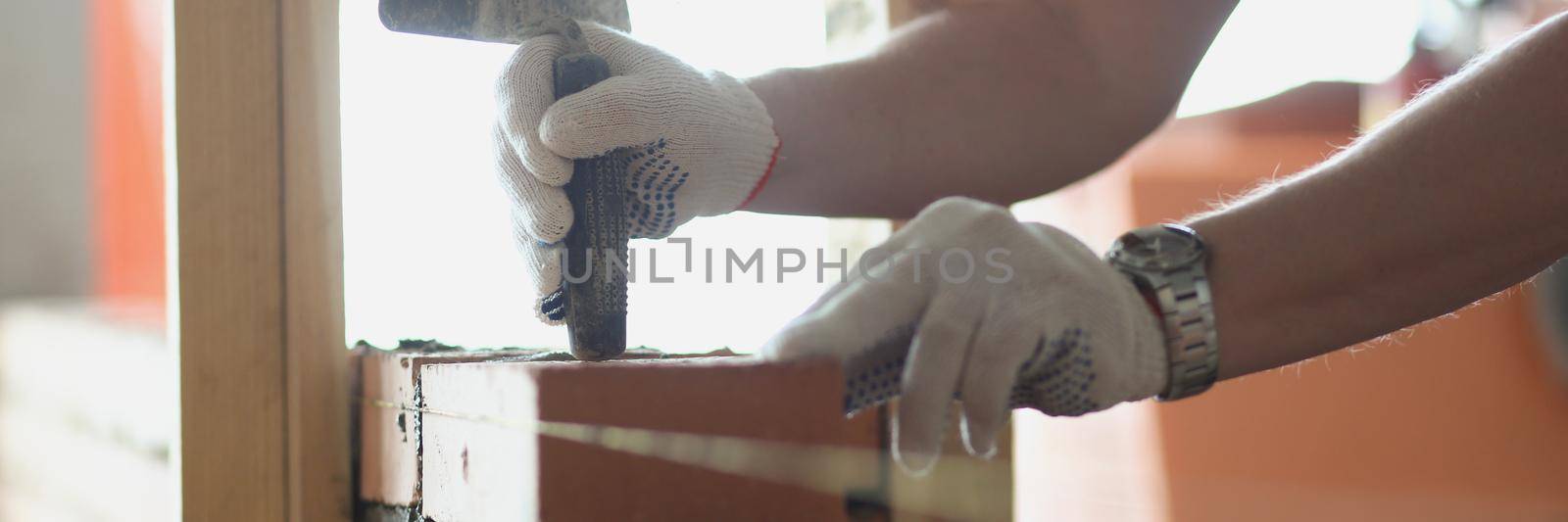 Close-up of foreman use special tool working with brick building wall in room. Progress on construction site, man busy at work. Renovation, builder concept