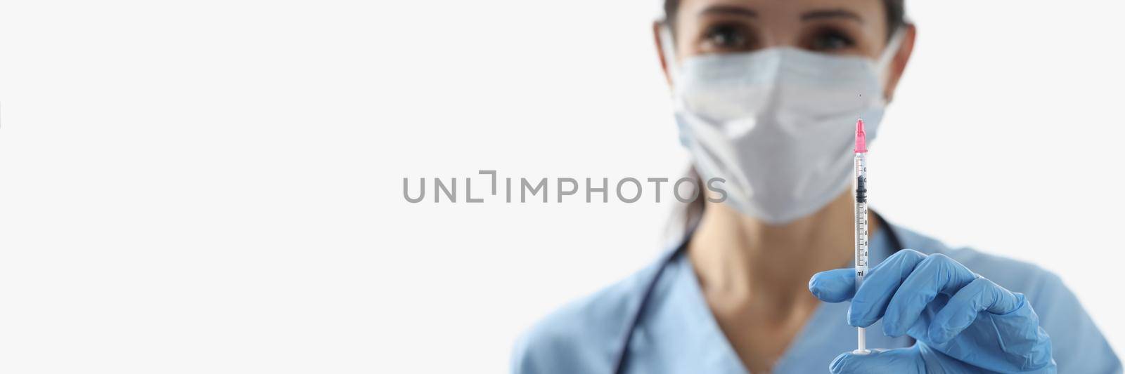 Close-up of female nurse holding syringe with vaccine liquid wear face mask. Doctor and cure vaccine from dangerous virus. Medicine, healthcare concept