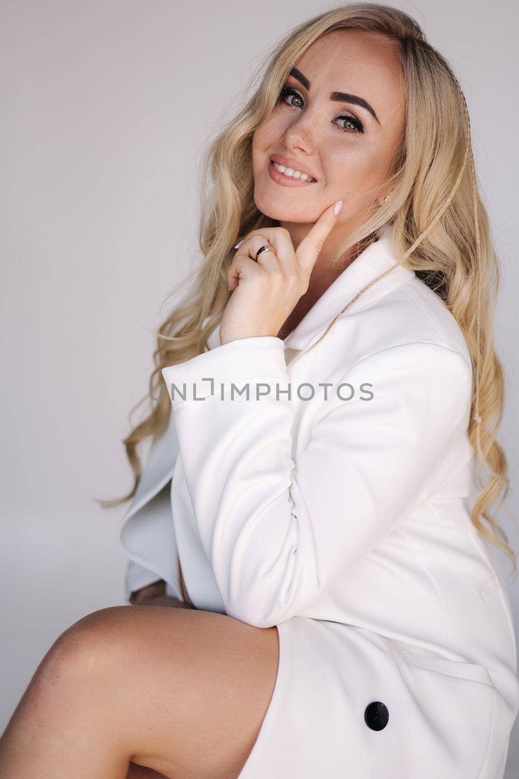 Close up portrait of pregnant woman in studio on white background. Beautiful future mother put her her hands on her belly. Stylish woman in white jaket.