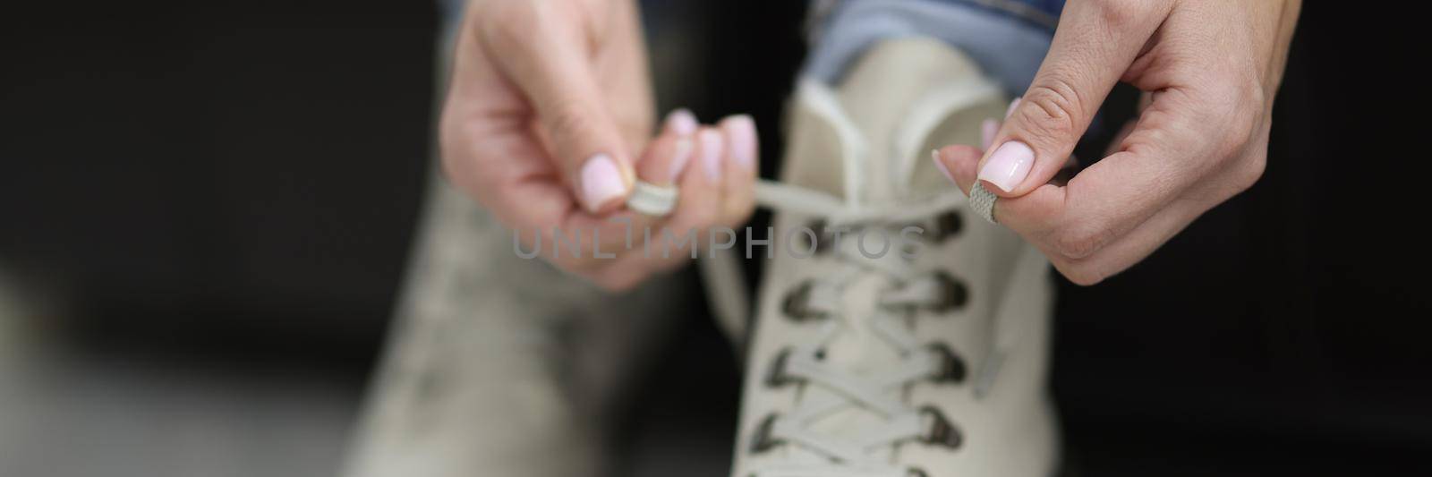 Close-up of woman put her white boots on and tie laces before going out. Fashion beige leather winter footwear. Footgear, trendy, design, dress up concept