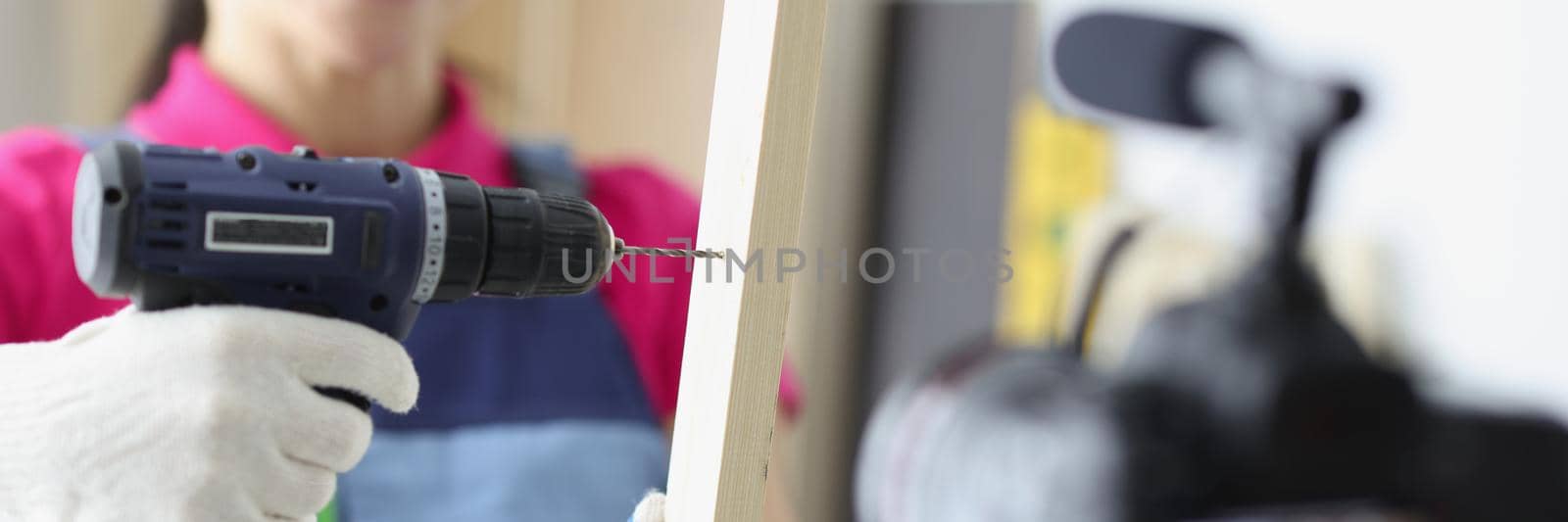 Close-up of happy woman construction site worker use drill to make hole in wooden plank. Film process on camera as educational lesson. Renovation concept