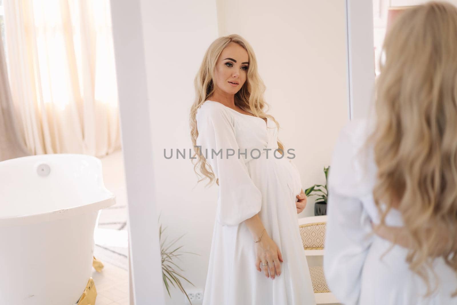 Beautiful portrait of pregnant woman in white dress. Concept of perfect pregnancy. Woman put her hand on belly. Future mother is waiting for baby.