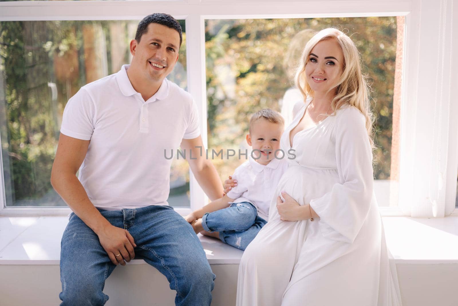 Happy photosession of pregnant woman her husband and their son. Family waiting for baby. White closes family look concept.