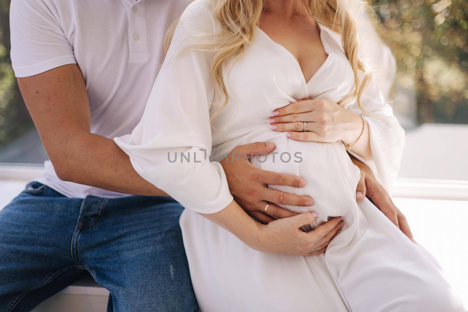 Middle selection of happy future parents of man and pregnant woman puts hands on belly and waiting for beby movement in the belly. Studio photosession.