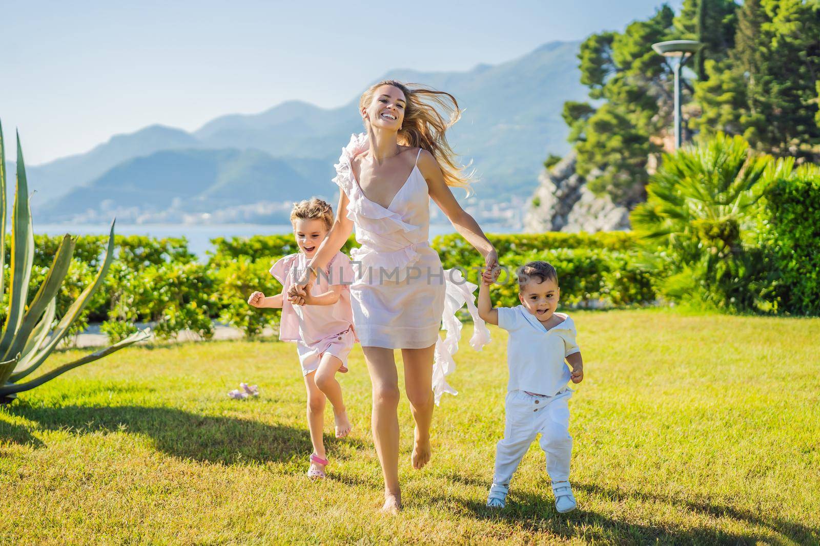 Joyful young mother playing catch together with two little children, boy and girl in green park on a summer day. Childhood, parenting, happiness concept by galitskaya