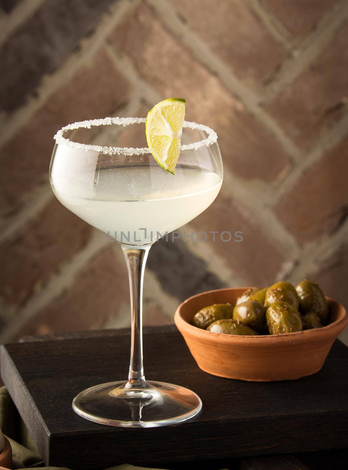 A vertical shot of a margarita cocktail and olives