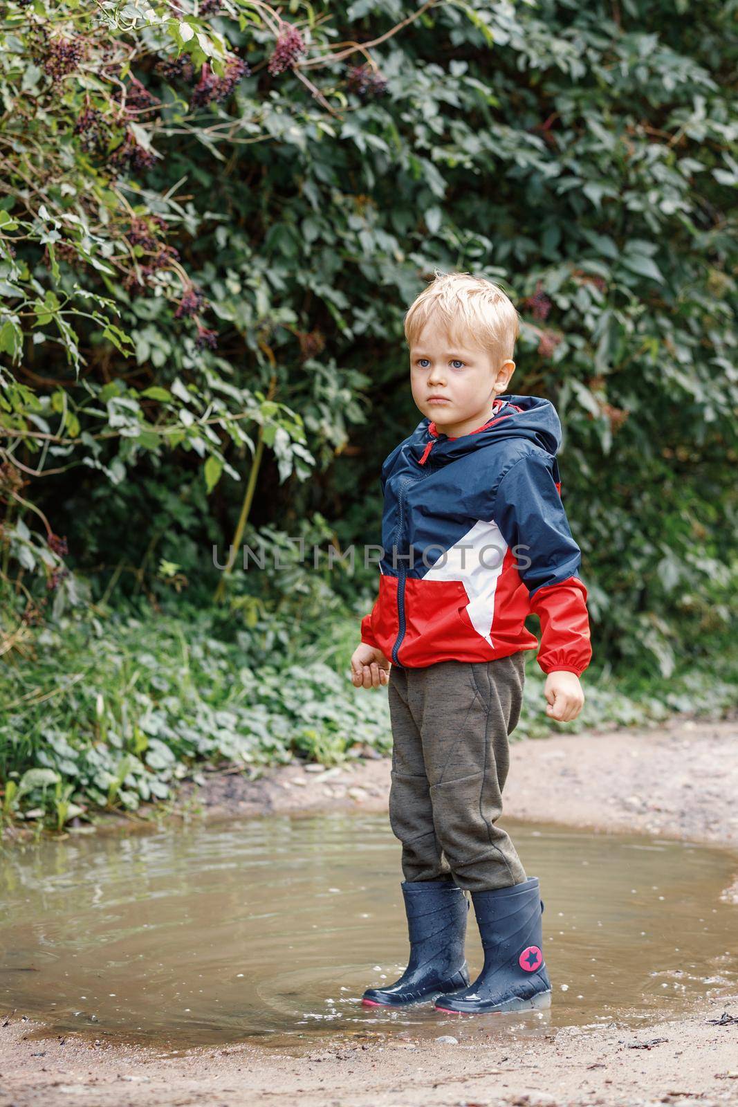 Kid playing autumn park. Outdoor fun by any weather. Standing In a Muddy Puddle.